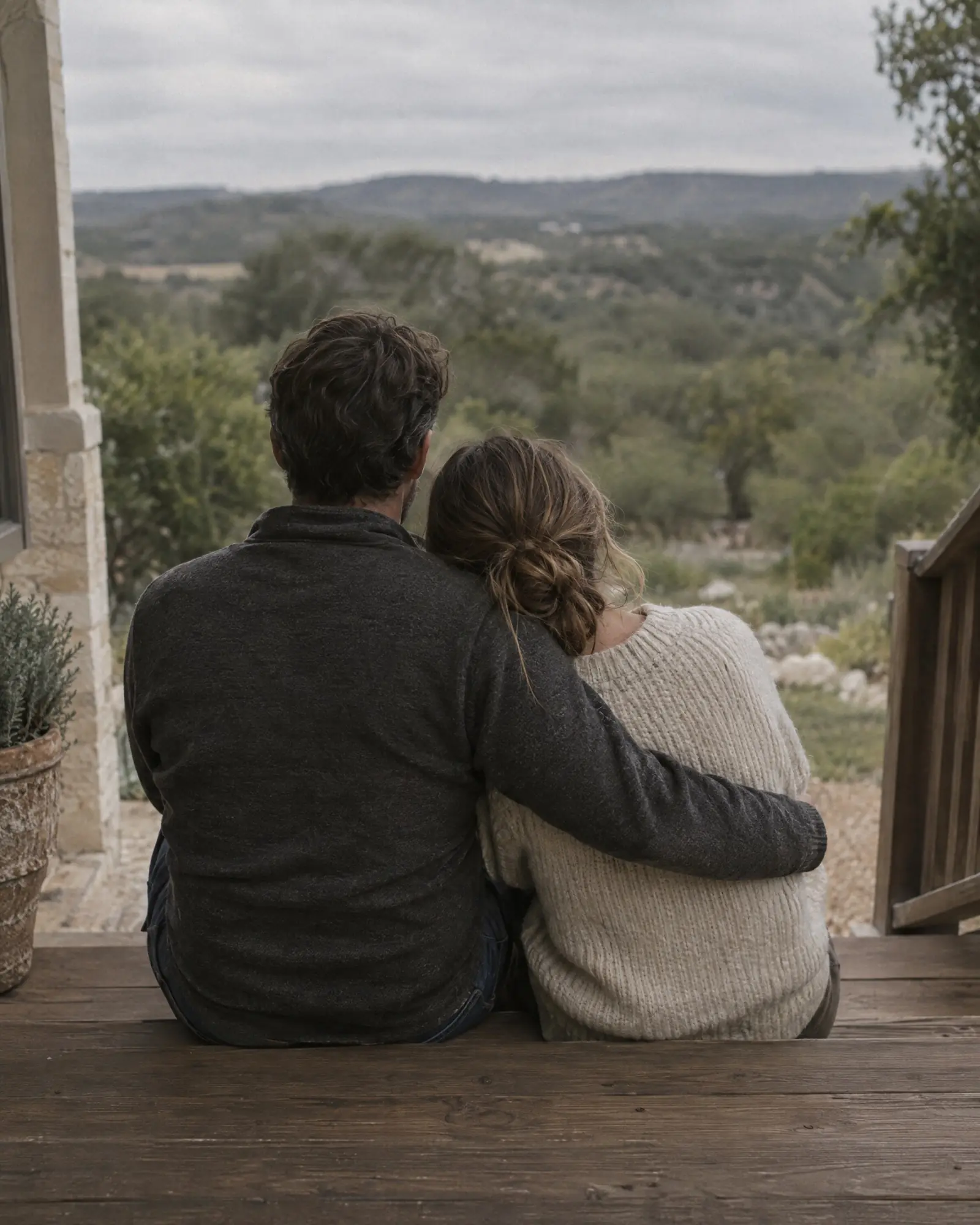 A couple seen from behind, sitting close together on a porch step overlooking green hills